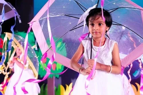 A child dancing with an umbrella on stage at the Crossmaze annual day